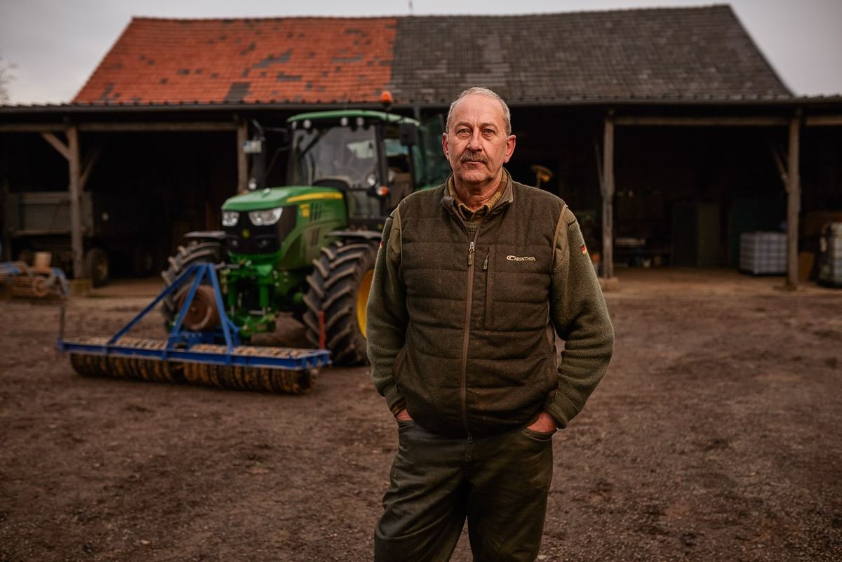 Portrait de céréalier dans la cour de sa ferme, tracteur au second plan